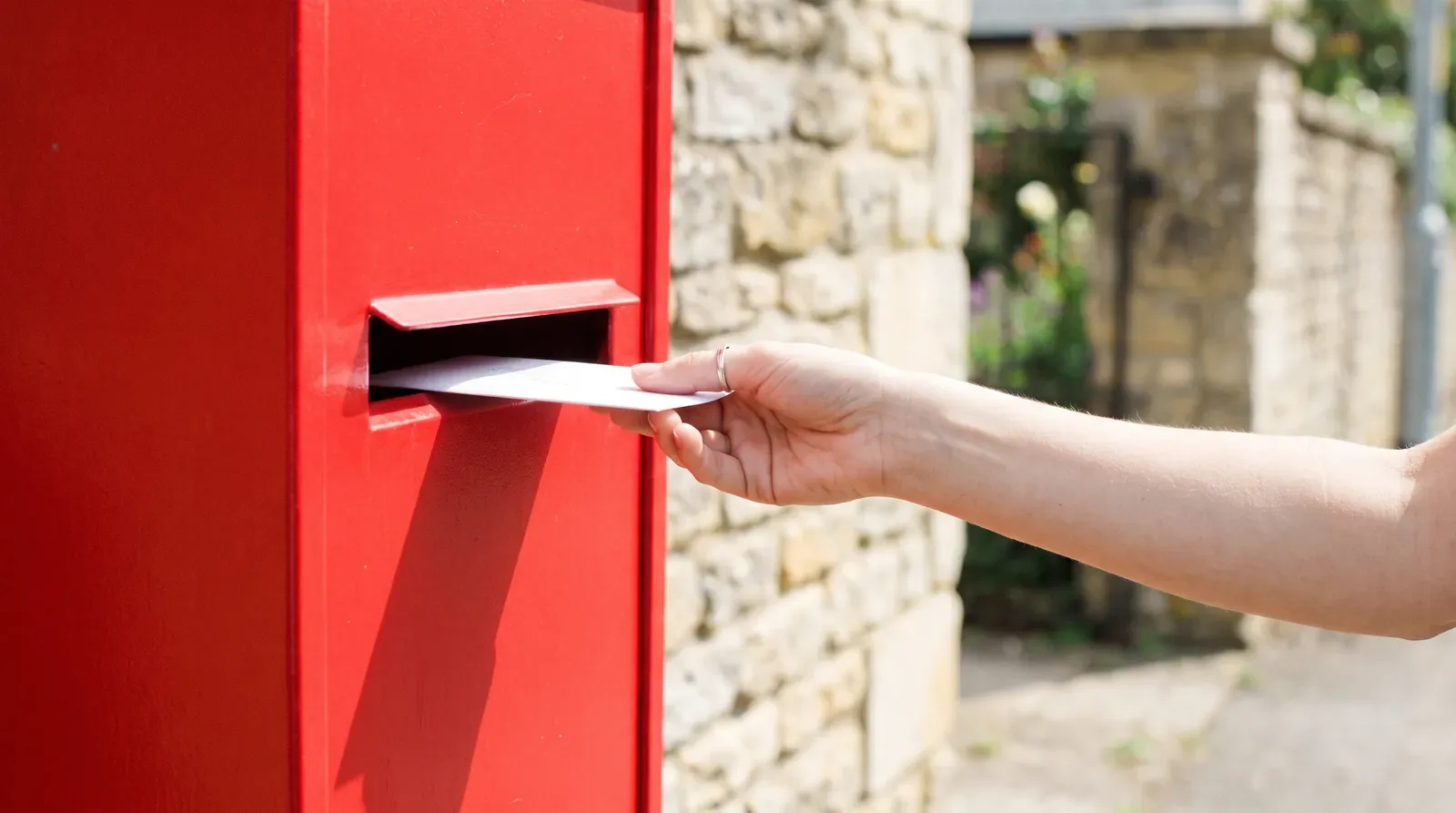 A hand posting a letter into a mailbox